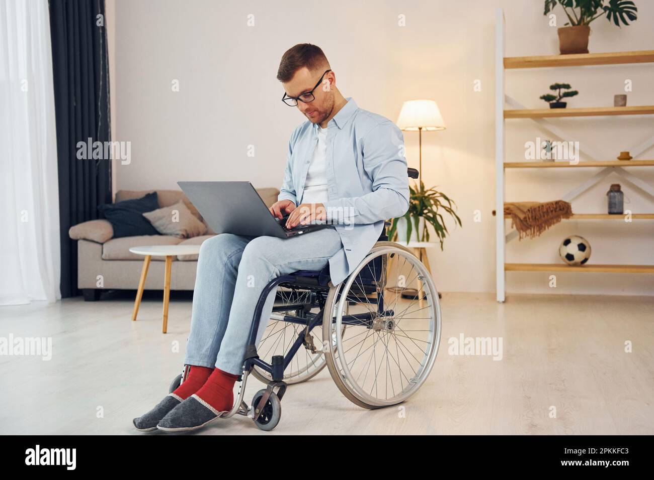 Avec ordinateur portable sur les jambes. Un homme handicapé en fauteuil  roulant est à la maison Photo Stock - Alamy