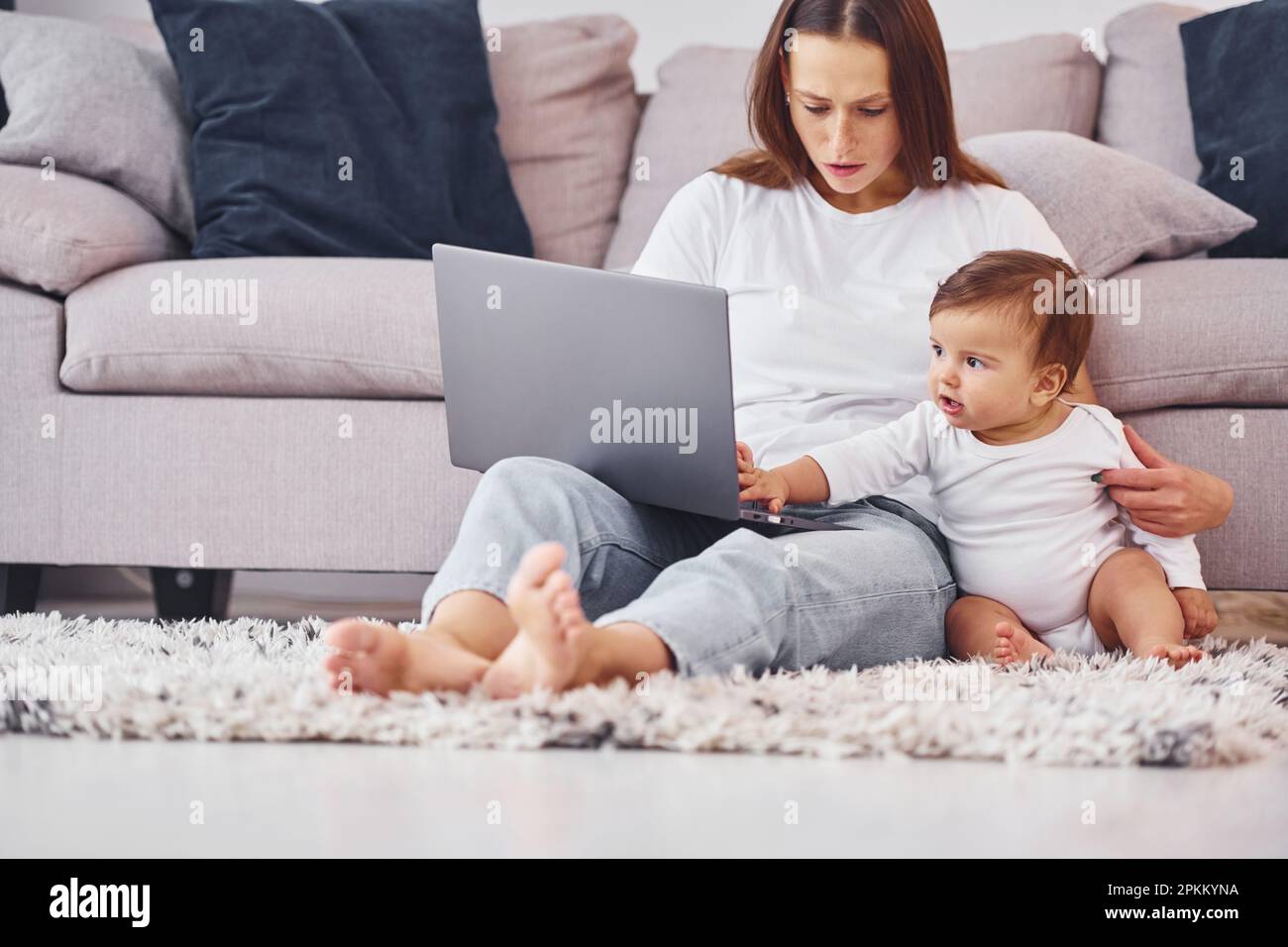 Utilisation d'un ordinateur portable. Mère avec sa petite fille est à l'intérieur à la maison ensemble. Banque D'Images