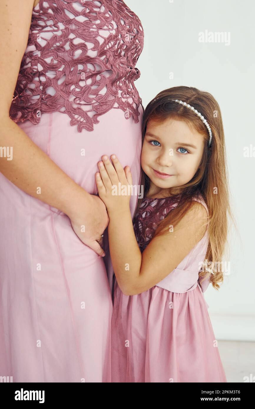 Conception de l'anticipation. Mère enceinte. Femme en robe debout avec sa fille dans le studio avec fond blanc. Banque D'Images