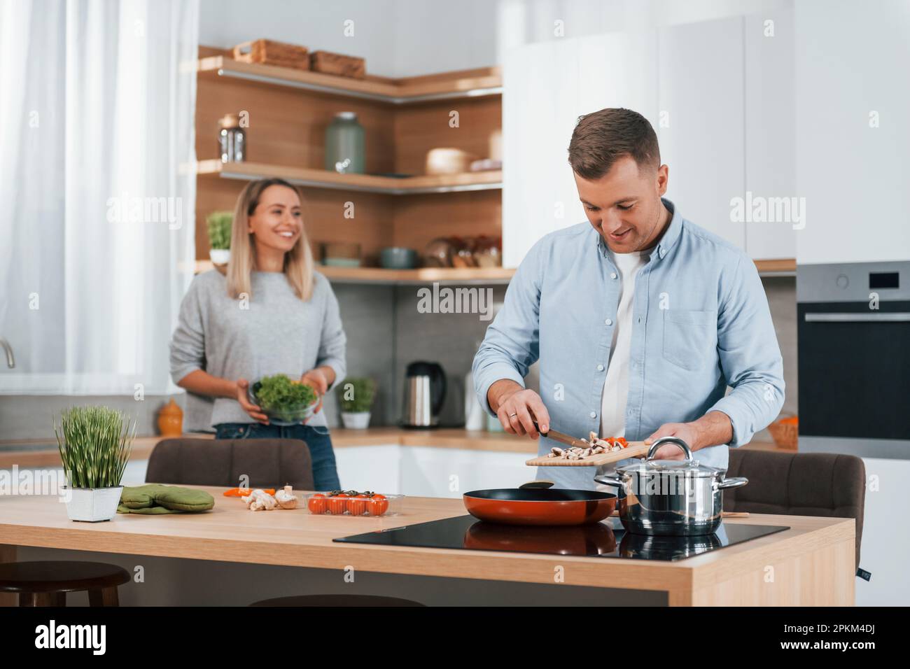S'entraider. Couple préparant la nourriture à la maison sur la cuisine moderne. Banque D'Images