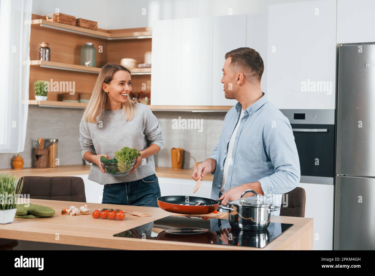 Parler les uns avec les autres. Couple préparant la nourriture à la maison sur la cuisine moderne. Banque D'Images