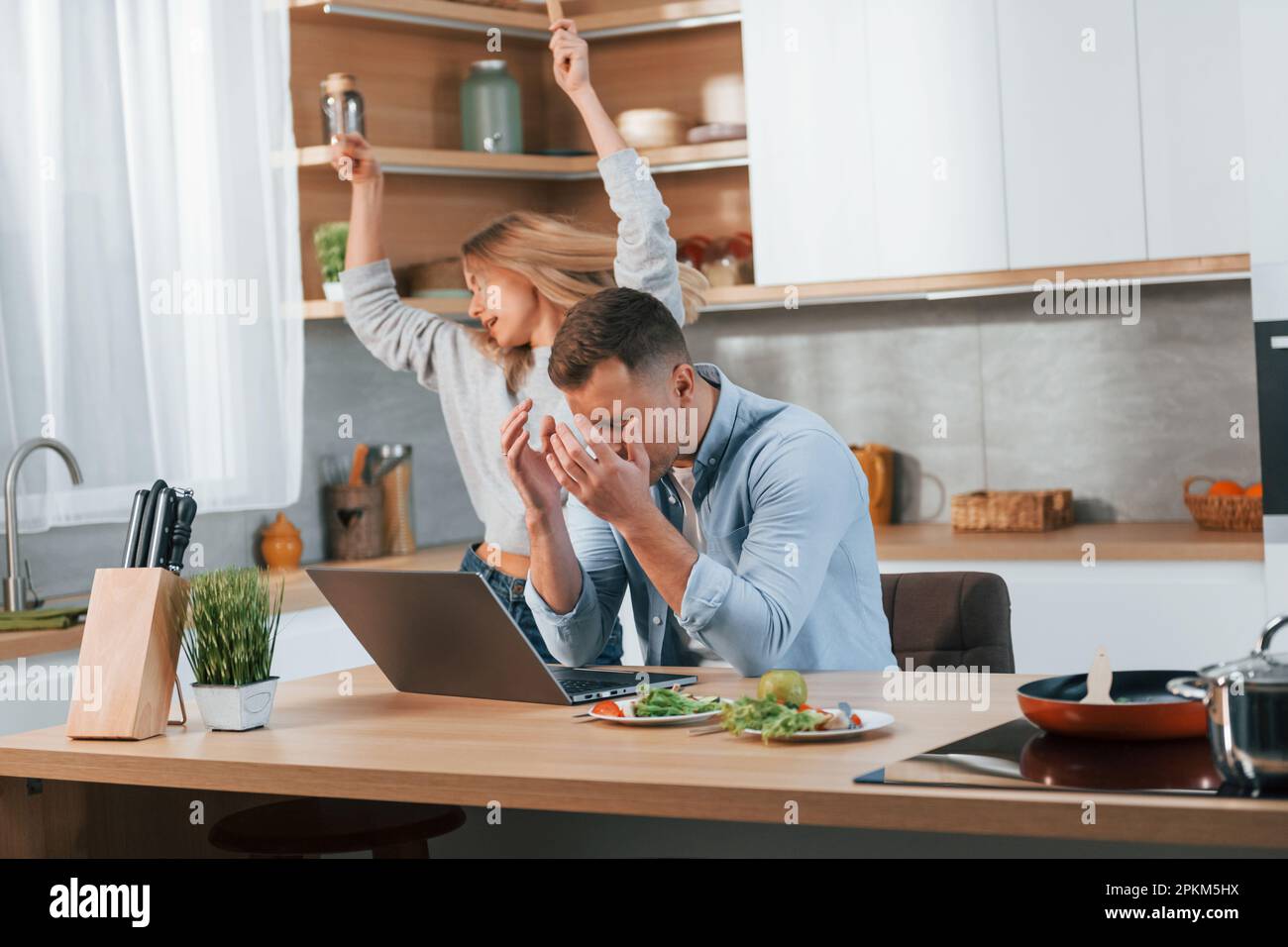 Ordinateur portable moderne sur la table. Couple préparant la nourriture à la maison sur la cuisine moderne. Banque D'Images