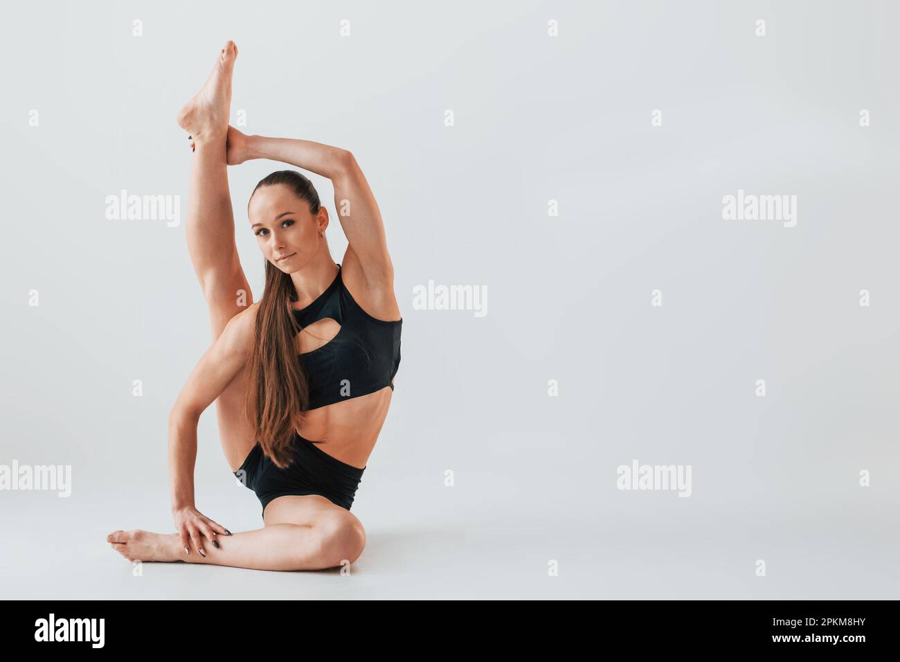 Flexibilité du corps. Jeune femme en vêtements de sport faisant de la gymnastique à l'intérieur. Banque D'Images