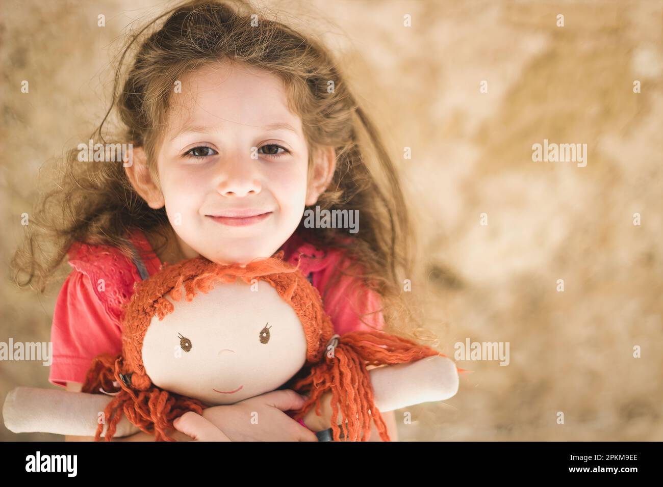 Une adorable petite fille blanche de race blanche tient avec amour une poupée de chiffon chérie avec des cheveux de gingembre Banque D'Images