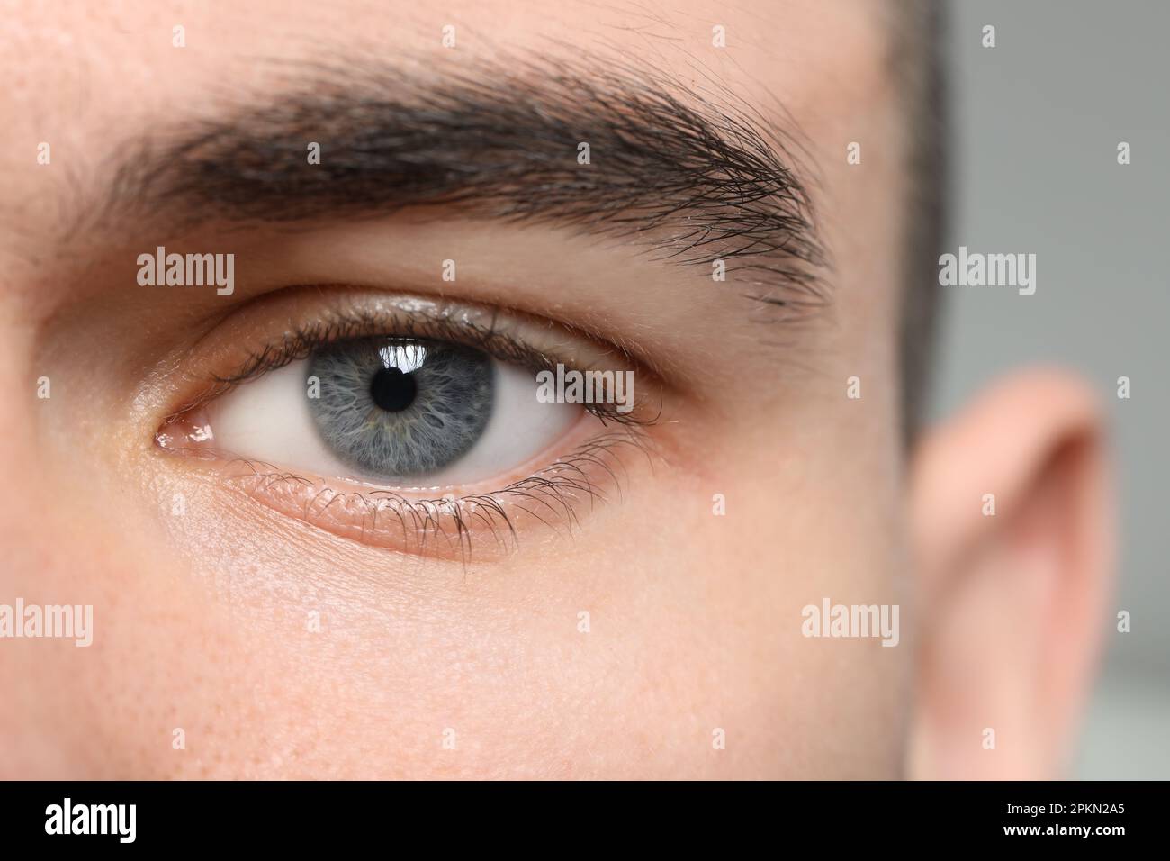 Gros plan d'un jeune homme avec de beaux yeux gris sur un arrière-plan flou Banque D'Images