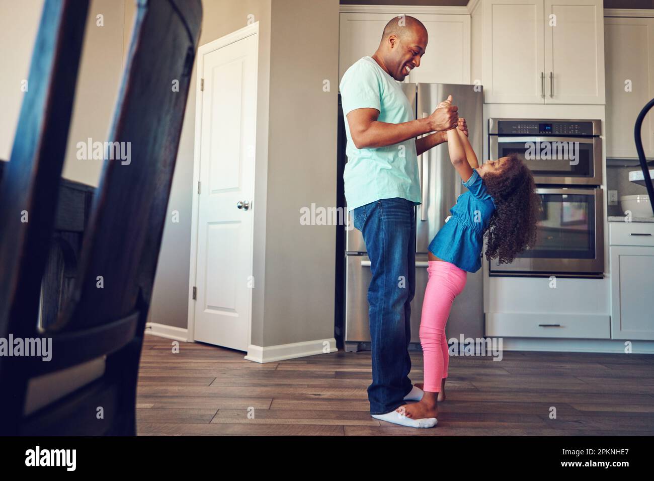 Cette famille sait s'amuser. une petite fille heureuse équilibrant sur les pieds de ses pères pendant qu'ils marchent dans la cuisine ensemble. Banque D'Images