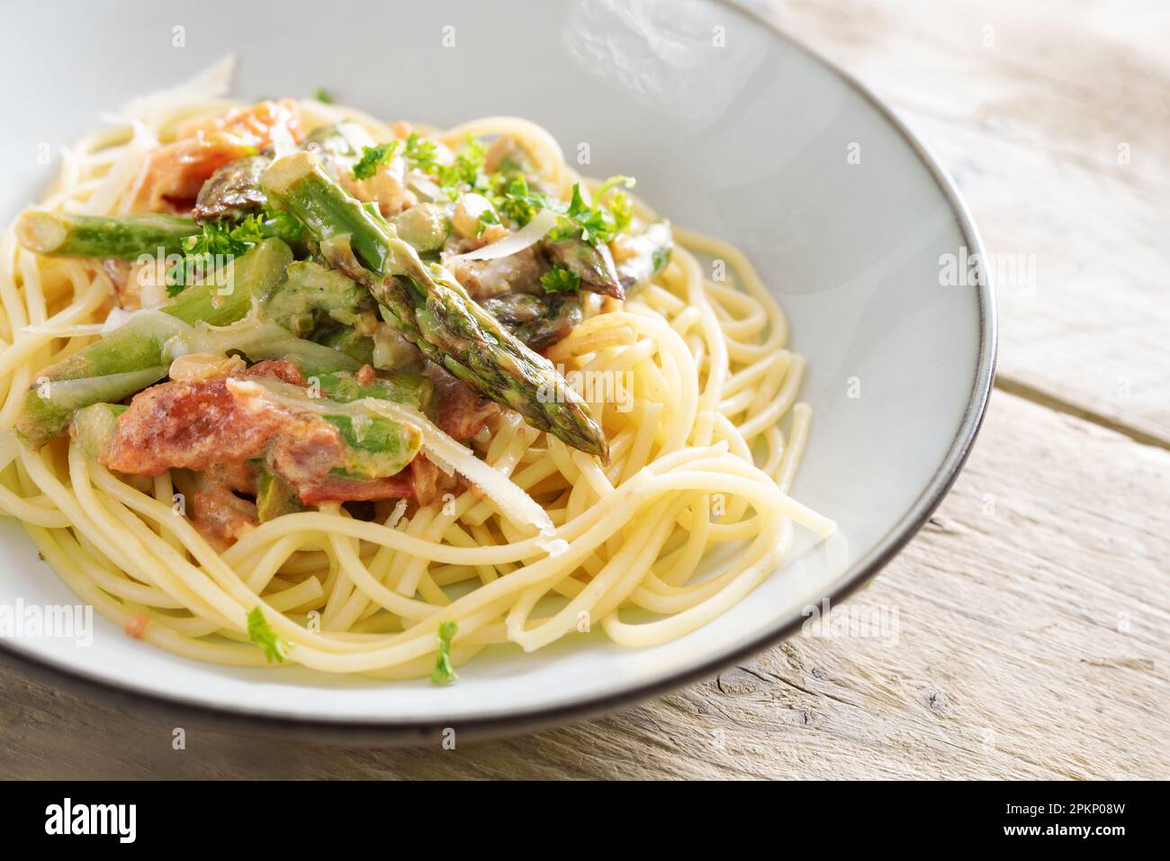 Asperges vertes en sauce tomate sur spaghetti au parmesan et persil dans une assiette gris clair sur une table rustique en bois, espace de photocopie, sélection de f Banque D'Images