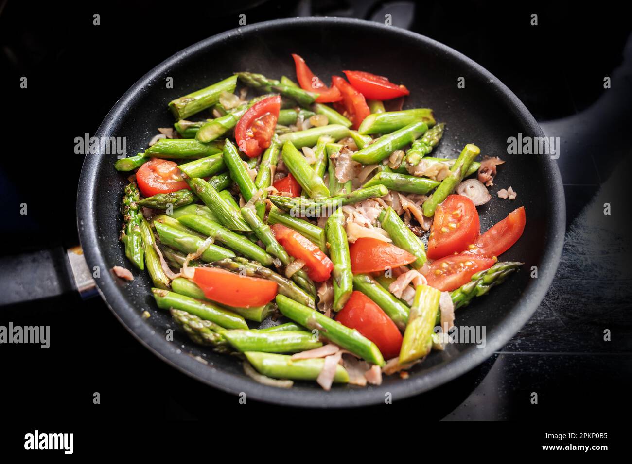 Asperges vertes, tomates et jambon de Parme dans une poêle noire sur le dessus de la cuisinière, la cuisson d'un repas de printemps sain, foyer choisi, profondeur étroite de fie Banque D'Images