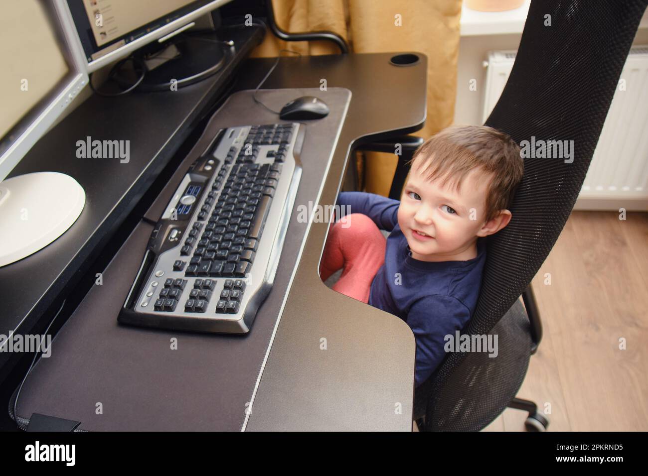 Bébé travaille sur un ordinateur équipé d'un clavier et d'une souris.  L'enfant heureux s'assoit sur une chaise d'ordinateur à côté des moniteurs  de PC. Enfant âgé d'un an neuf mois Photo Stock -