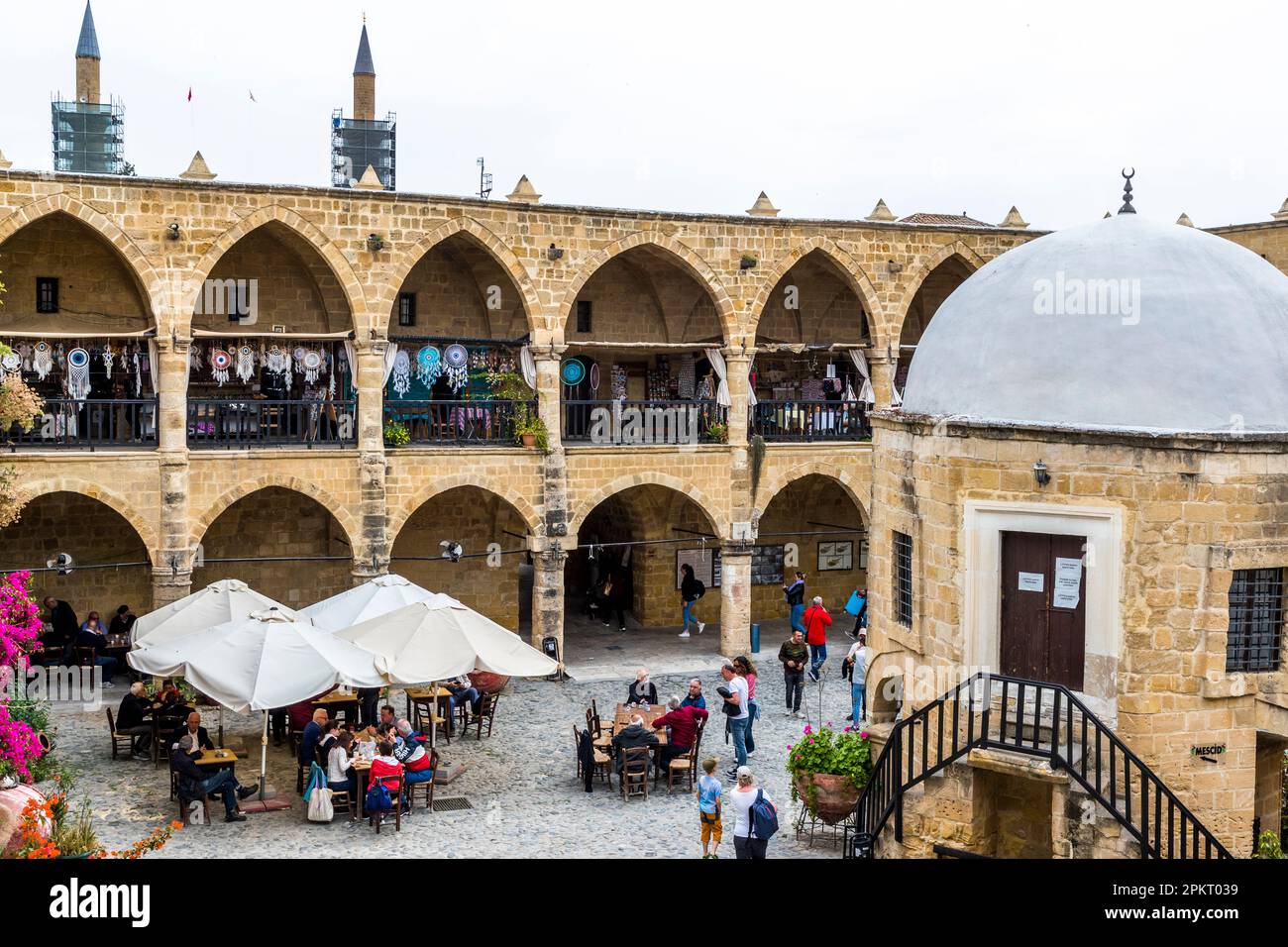 La cour du Büyük Han (Grande Auberge) à Lefkoşa/Nicosia, République turque de Chypre du Nord (RTNC), abritait autrefois des marchands voyageurs. Muzaffer Pasha, le premier dirigeant ottoman de Chypre, a fait construire la caravanseraille à deux étages en 1572. Une petite mosquée à dôme avec une fontaine pour l'ablution rituelle avant la prière se dresse dans la cour, entourée de tables de café sous des parasols. À l'arrière-plan, les minarets de la mosquée Selimiye voisine sont probablement visibles. Le Büyük Han est considéré comme l'un des plus beaux bâtiments de Chypre. Banque D'Images