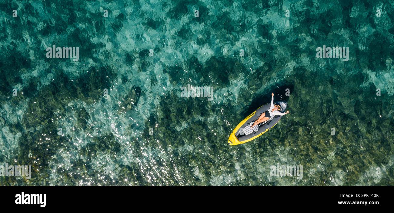 Une femme solitaire dans un chapeau de paille souriant, reposant couché flottant dans un kayak sur les vagues turquoises de la mer Adriatique. Vue aérienne du dessus de la côte. Exotique c Banque D'Images