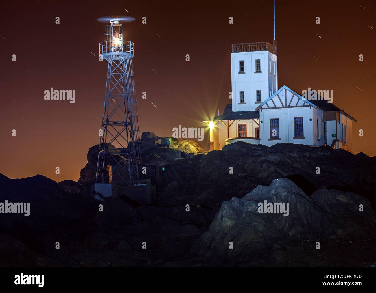 Les lumières de la ville de Lüderitz reflètent une lueur rouge sinistre dans le ciel nocturne au-dessus du phare de Shark Island. Banque D'Images