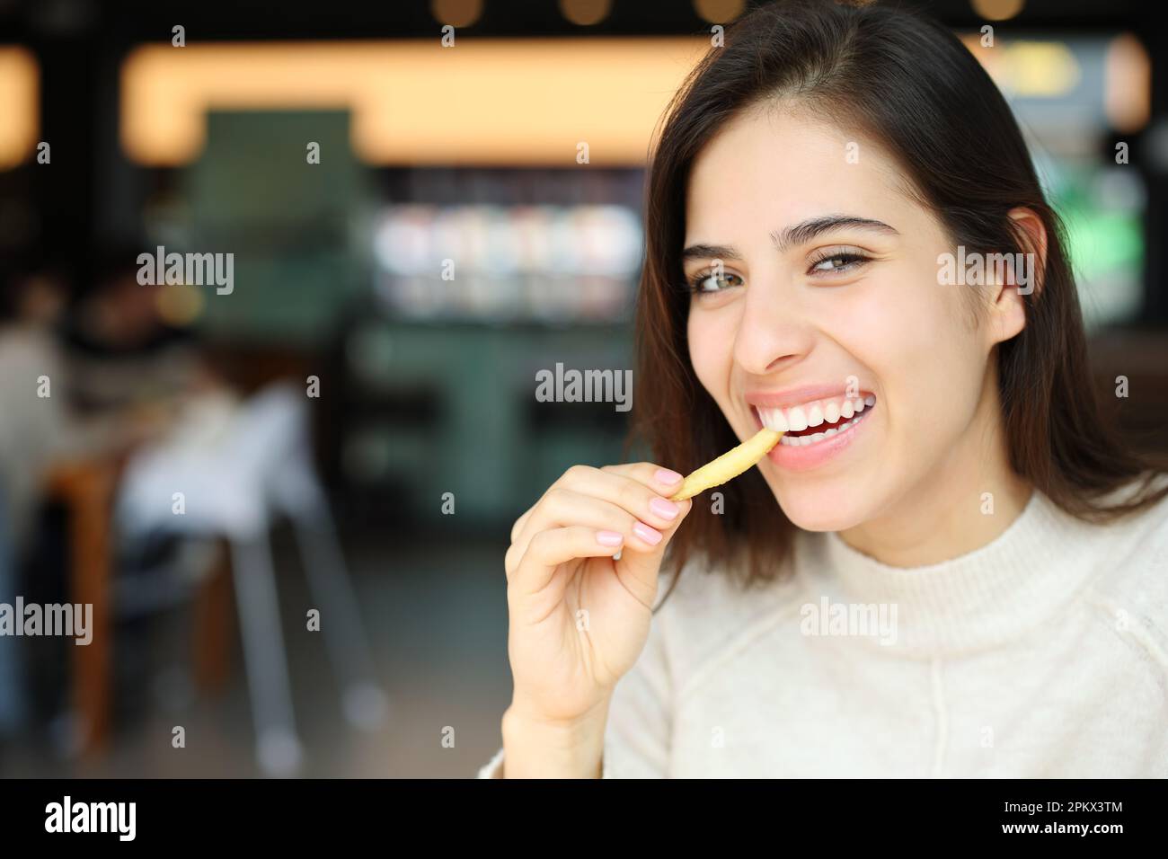 Bonne femme mangeant des frites en regardant un appareil photo dans un restaurant Banque D'Images