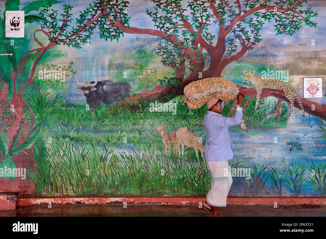 Un porteur avec un sac sur sa tête passe une fresque à la gare de Byculla à Mumbai, en Inde, son thème de la faune un hommage au zoo de Byculla voisin Banque D'Images