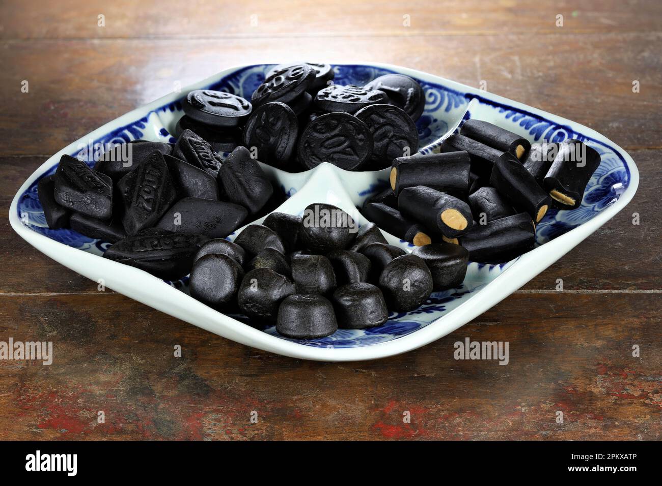 Bonbons de réglisse hollandais sur une plaque de Delftware sur fond en bois Banque D'Images