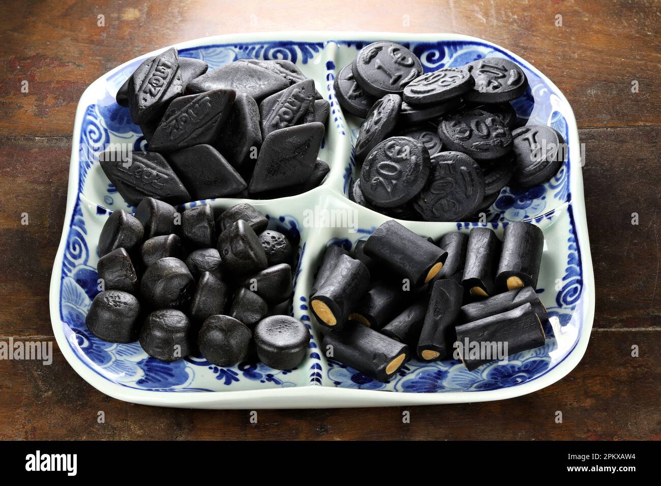Bonbons de réglisse hollandais sur une plaque de Delftware sur fond en bois Banque D'Images