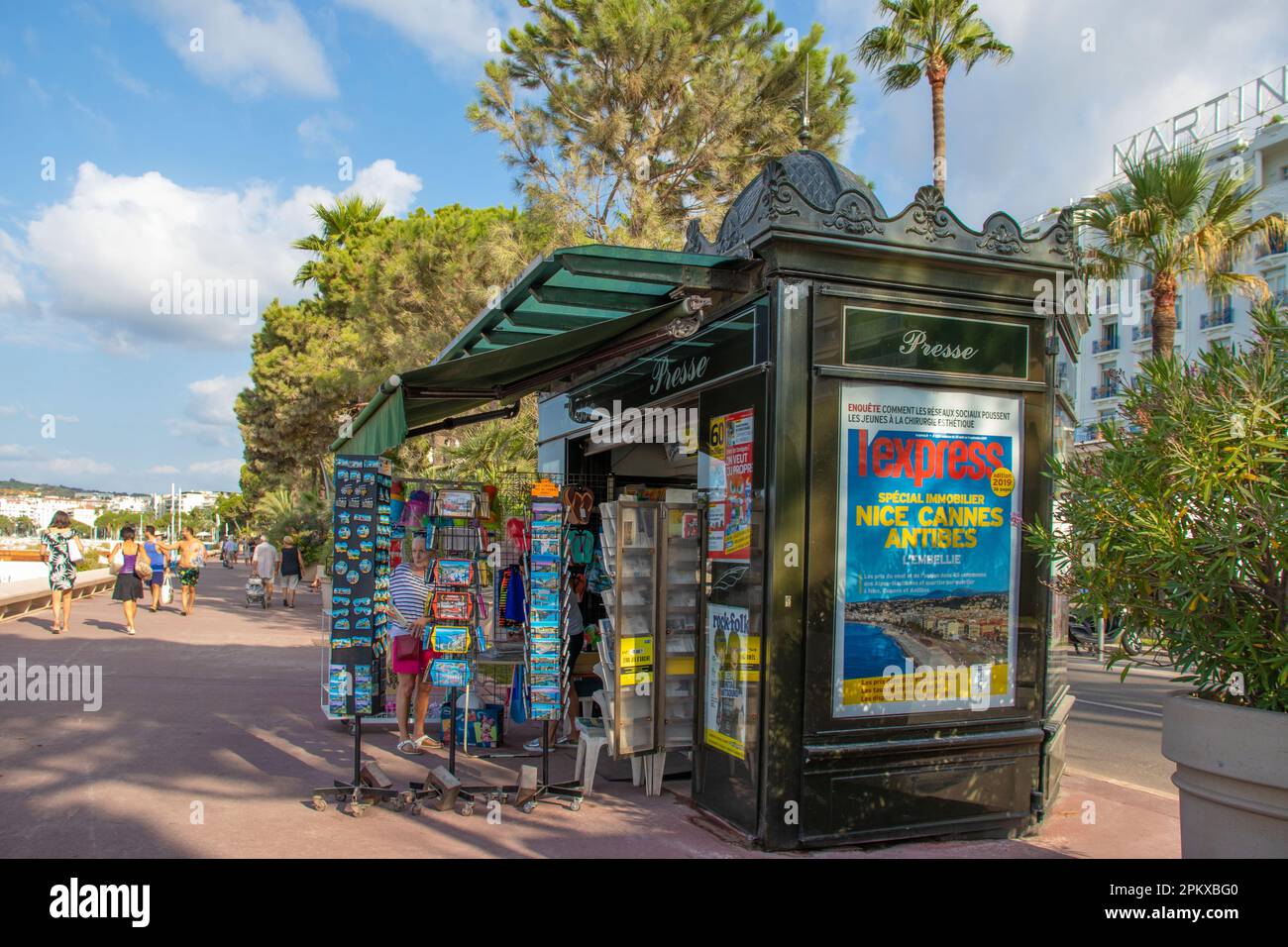 Un kiosque carte postale et souvenir sur la promenade le long du front de mer de la Croisette à Cannes, dans le sud de la France, avec le bâtiment blanc de l'hôtel Mar Banque D'Images