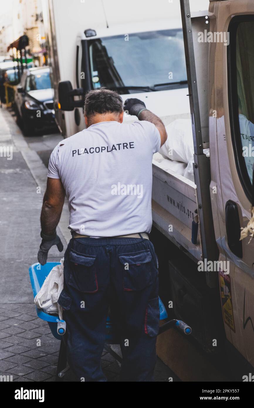 Un employé de Placoplatre dépose des sacs blancs d'un camion sur un chariot à une roue Banque D'Images