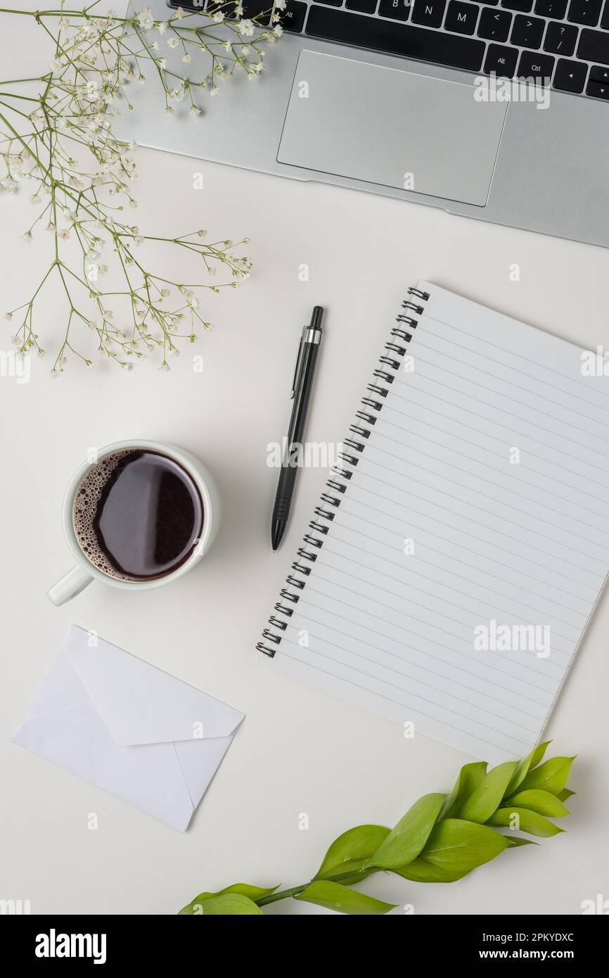 Bureau avec table et vue sur le dessus. Espace de travail avec tableau à pinces vierge, ordinateur portable, fournitures de bureau, crayon, feuille verte, et une tasse de café sur fond blanc Banque D'Images
