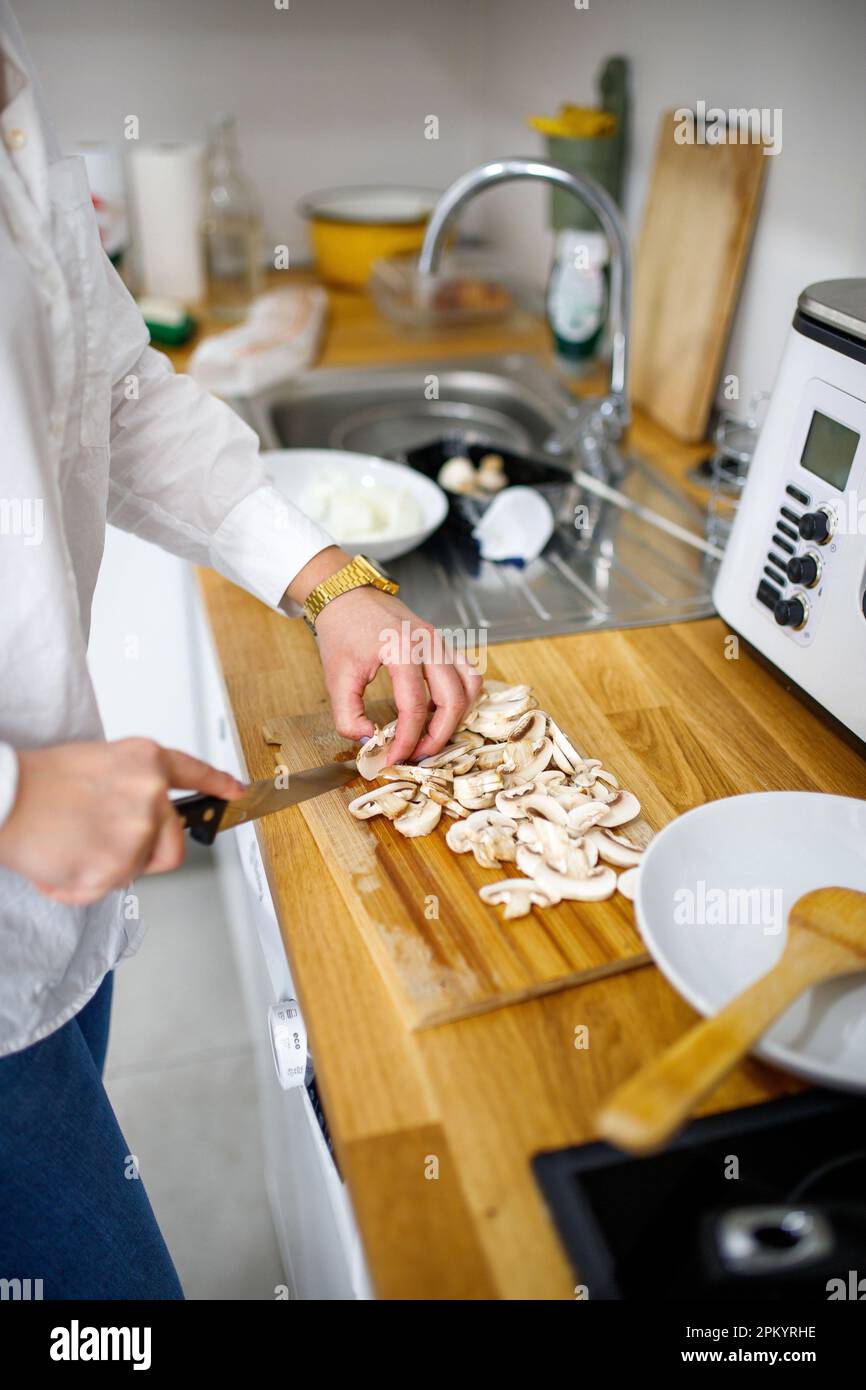 Vue latérale d'une chemise blanche anonyme située près du comptoir et coupant des champignons frais tout en cuisant le dîner dans la cuisine Banque D'Images