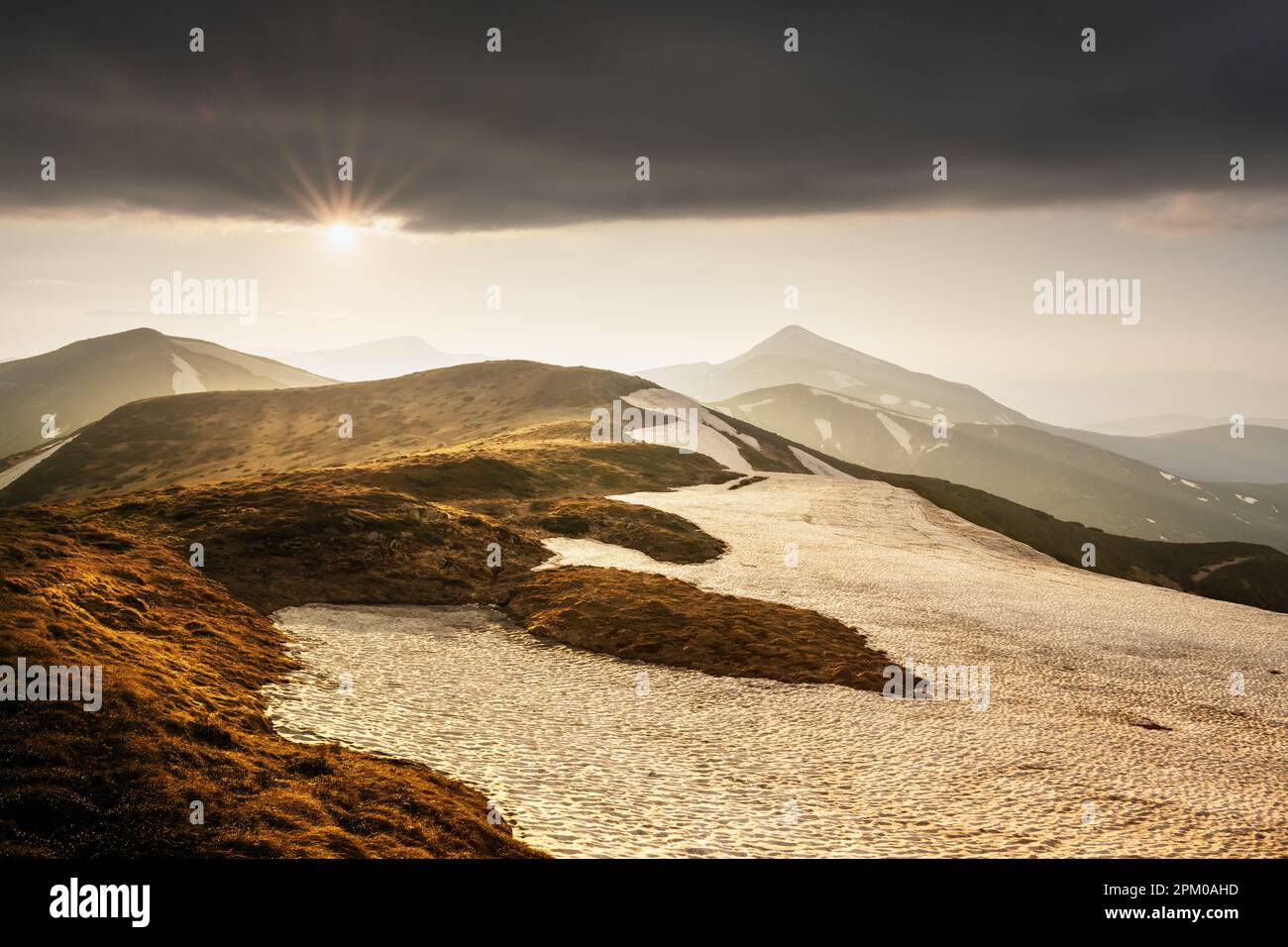 Vue sur les collines herbeuses avec des chaussettes orange et des montagnes enneigées en arrière-plan. Scène de printemps spectaculaire. Photographie de paysage Banque D'Images