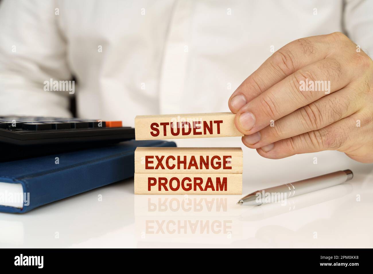 Concept d'entreprise. Dans les mains d'un homme d'affaires, blocs de bois avec l'inscription - Programme d'échange étudiant, à côté d'un bloc-notes et d'une calculatrice. Banque D'Images