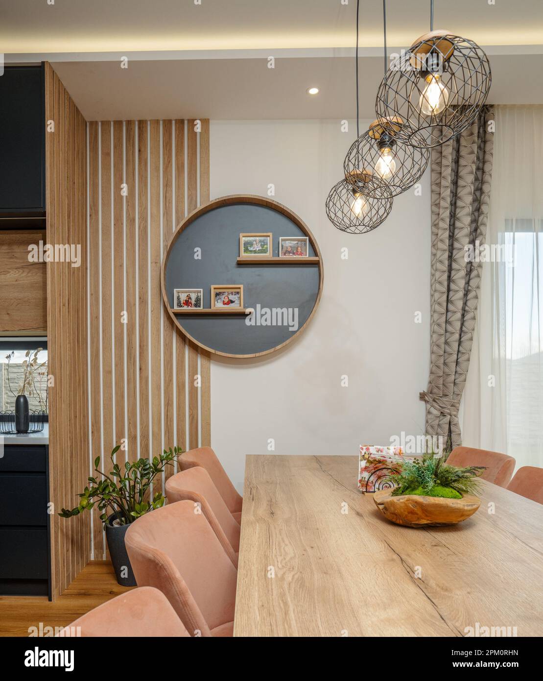 Une salle à manger moderne avec une table en bois, des chaises confortables, des lampes suspendues et des photos Banque D'Images