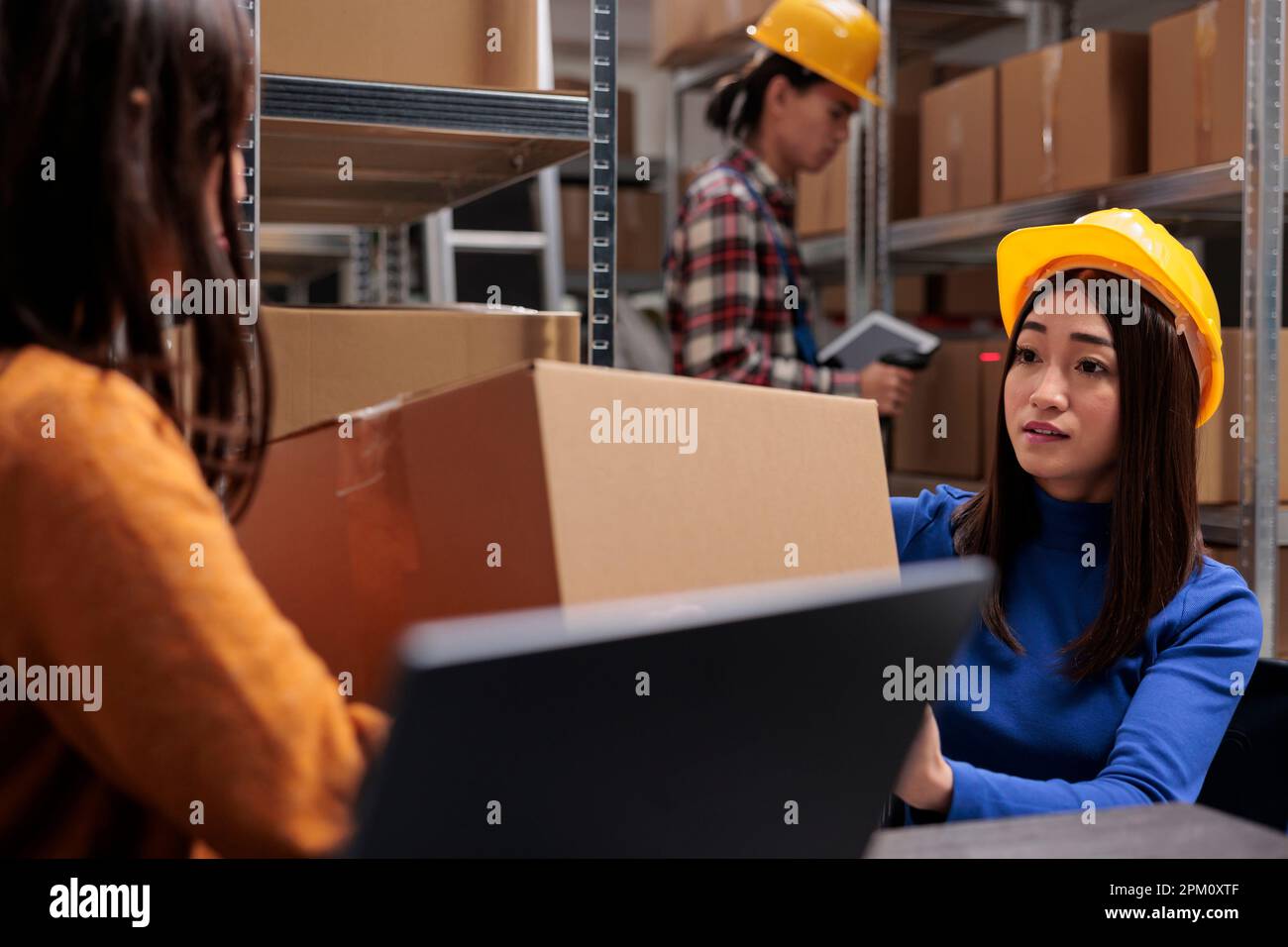 Collègues de l'entrepôt tenant la boîte et gérant les opérations logistiques de la chaîne d'approvisionnement tout en étant assis au bureau dans la salle de stockage. Le responsable du service postal et le préparateur de commande supervisent l'expédition Banque D'Images