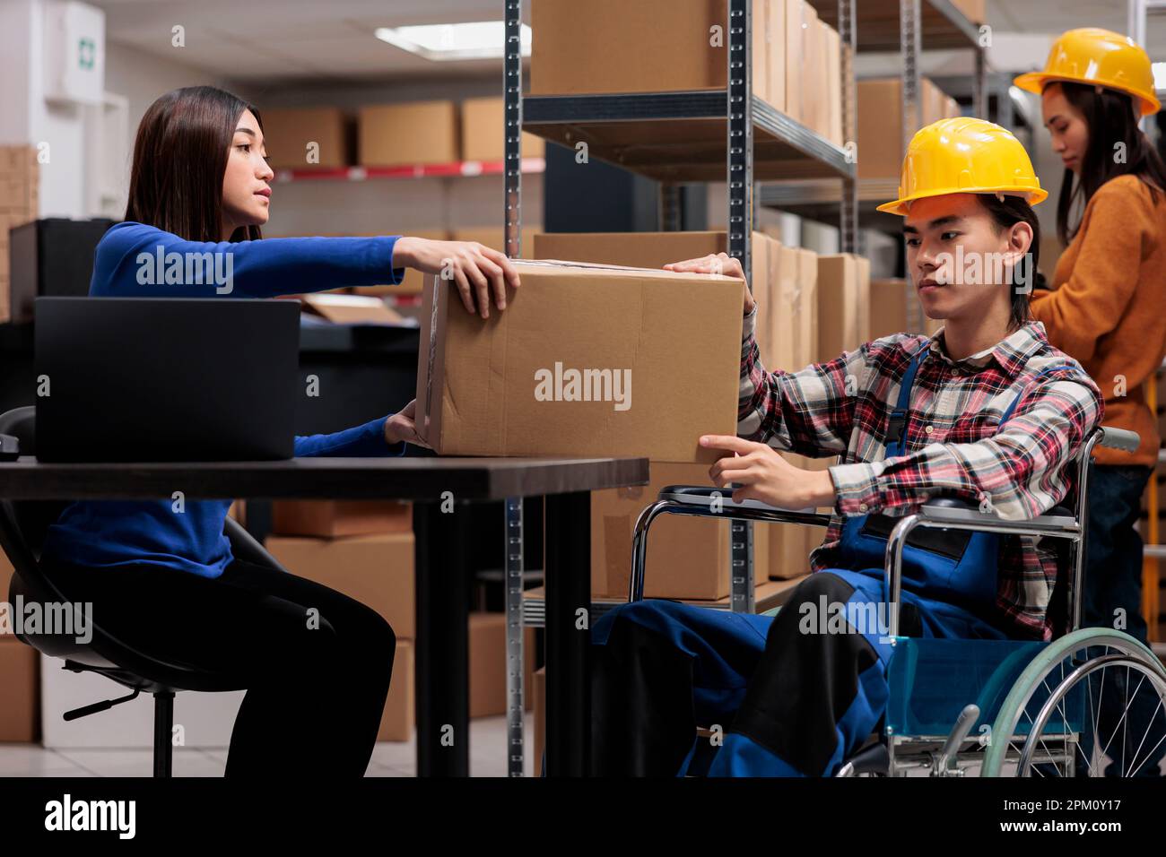 Opérateur d'entrepôt asiatique et préparateur de commande en fauteuil roulant, gérant la livraison des colis à la réception. Deux collègues du service postal traitant la boîte de carton de fret dans l'entrepôt Banque D'Images