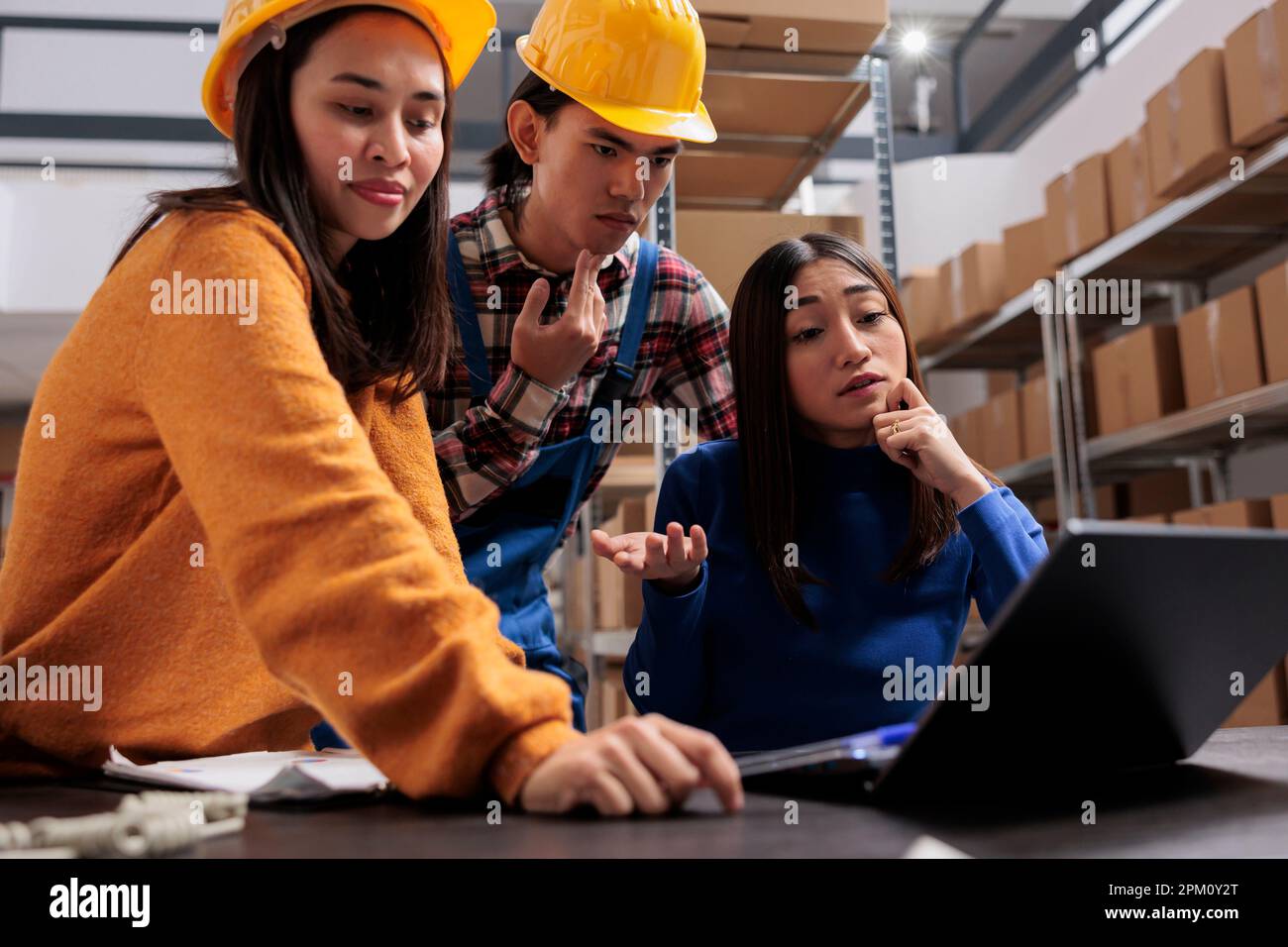 L'équipe des directeurs d'entrepôt asiatiques analyse la liste de contrôle d'expédition sur l'ordinateur portable tout en se tenant près du bureau. Les employés des magasins de détail vérifient le plan logistique sur l'ordinateur dans la salle de stockage Banque D'Images