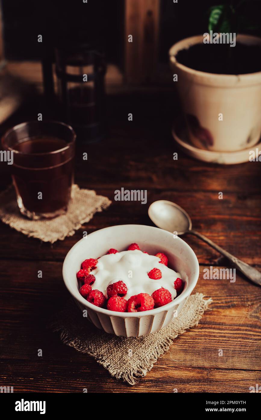 Bol de dessert d'été avec framboises mûres et yaourt grec et verre de café sur une surface en bois Banque D'Images