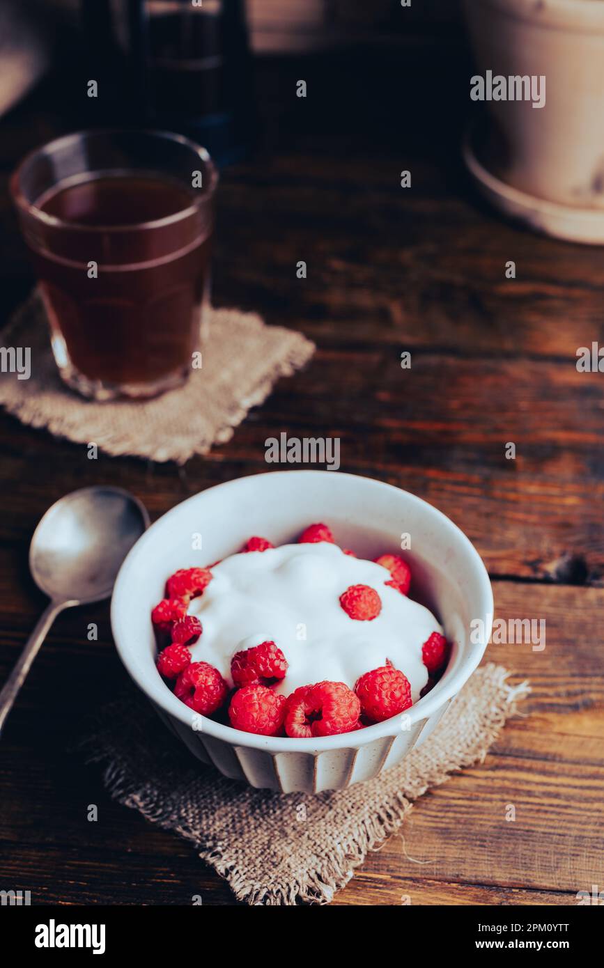 Bol de dessert d'été avec framboises mûres et yaourt grec et verre de café sur une surface en bois Banque D'Images