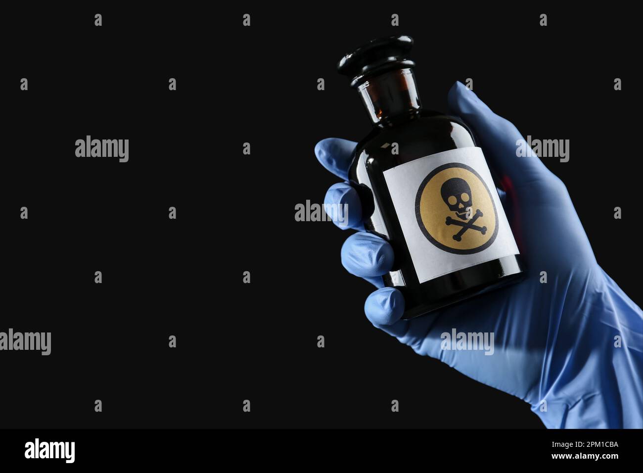 Femme en gants tenant une bouteille de poison en verre avec un panneau d'avertissement sur fond noir, gros plan. Espace pour le texte Banque D'Images