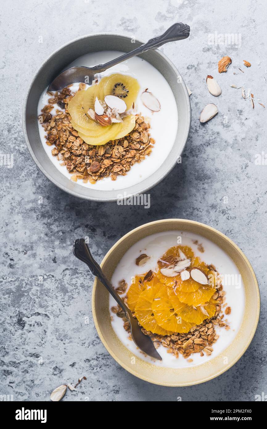 Bols de céréales au yaourt avec kiwi et fruits orange sur fond gris, vue du dessus. Repas végétarien sain pour le petit déjeuner Banque D'Images