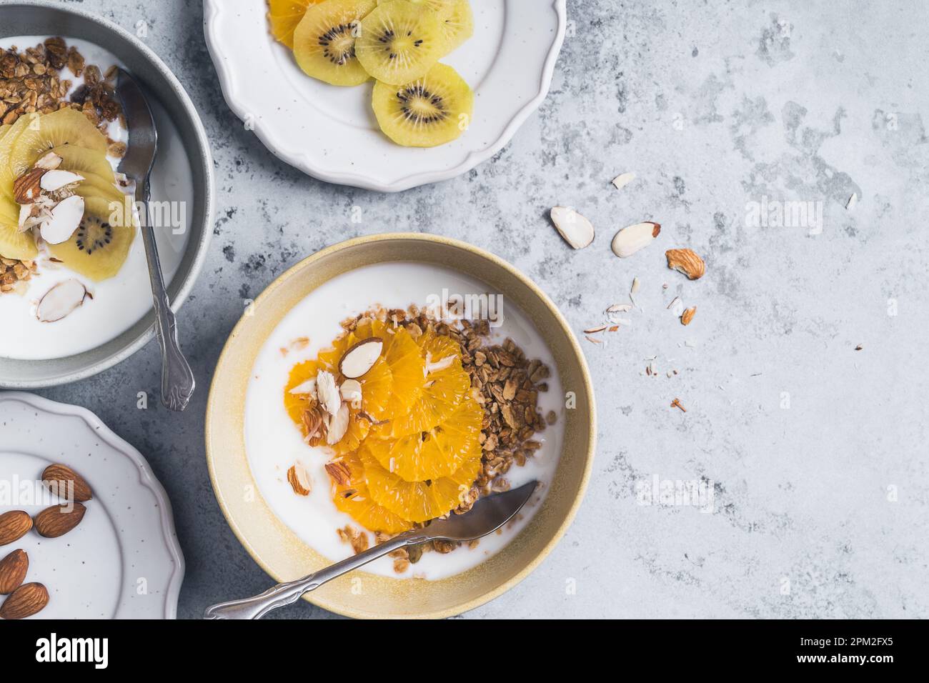 Bols de céréales au yaourt avec kiwi et fruits orange sur fond gris, vue du dessus. Repas végétarien sain pour le petit déjeuner Banque D'Images