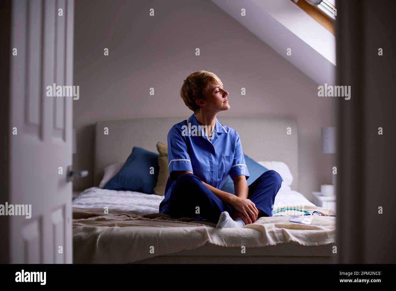 Femme réfléchie portant des infirmières ou des médecins uniforme assis sur le lit à la maison Banque D'Images