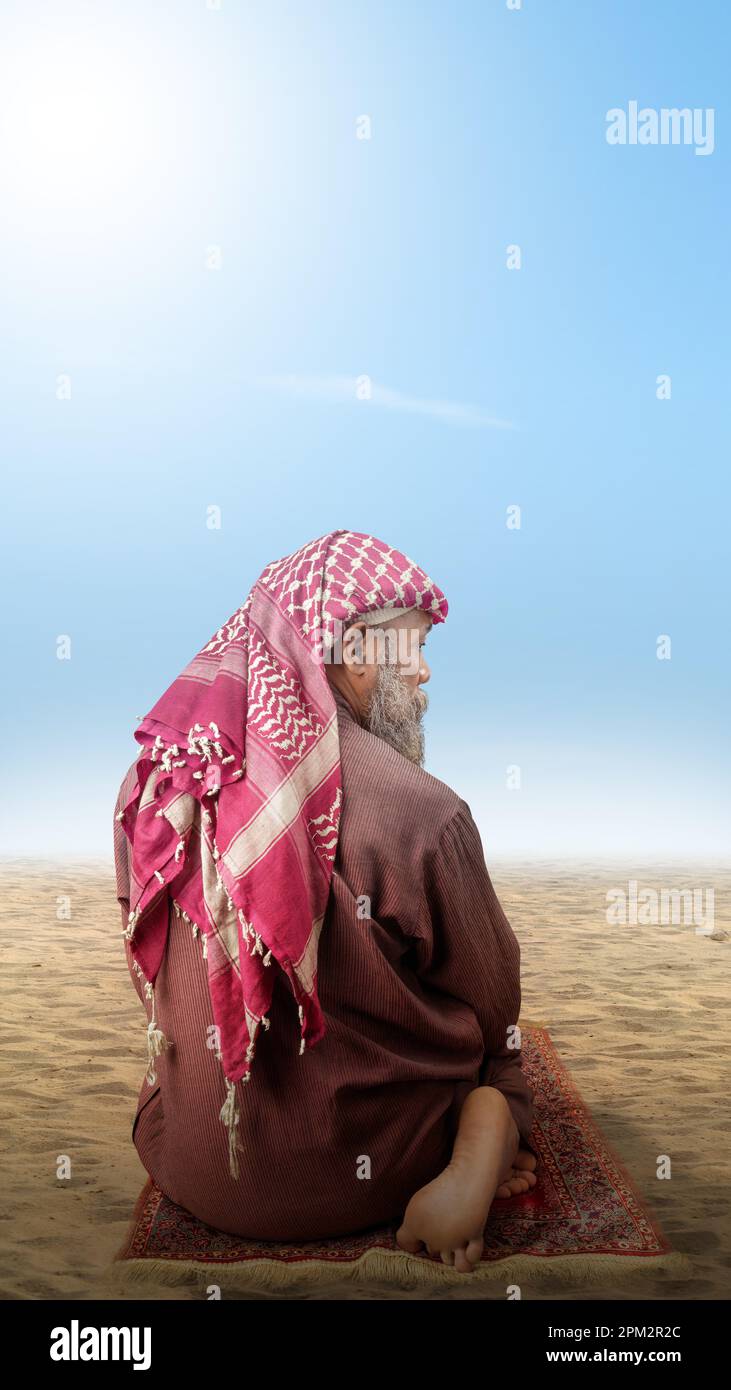 Homme musulman avec une barbe portant du keffiyeh avec agal en position de prière (salat) sur le tapis de prière avec le fond bleu du ciel Banque D'Images
