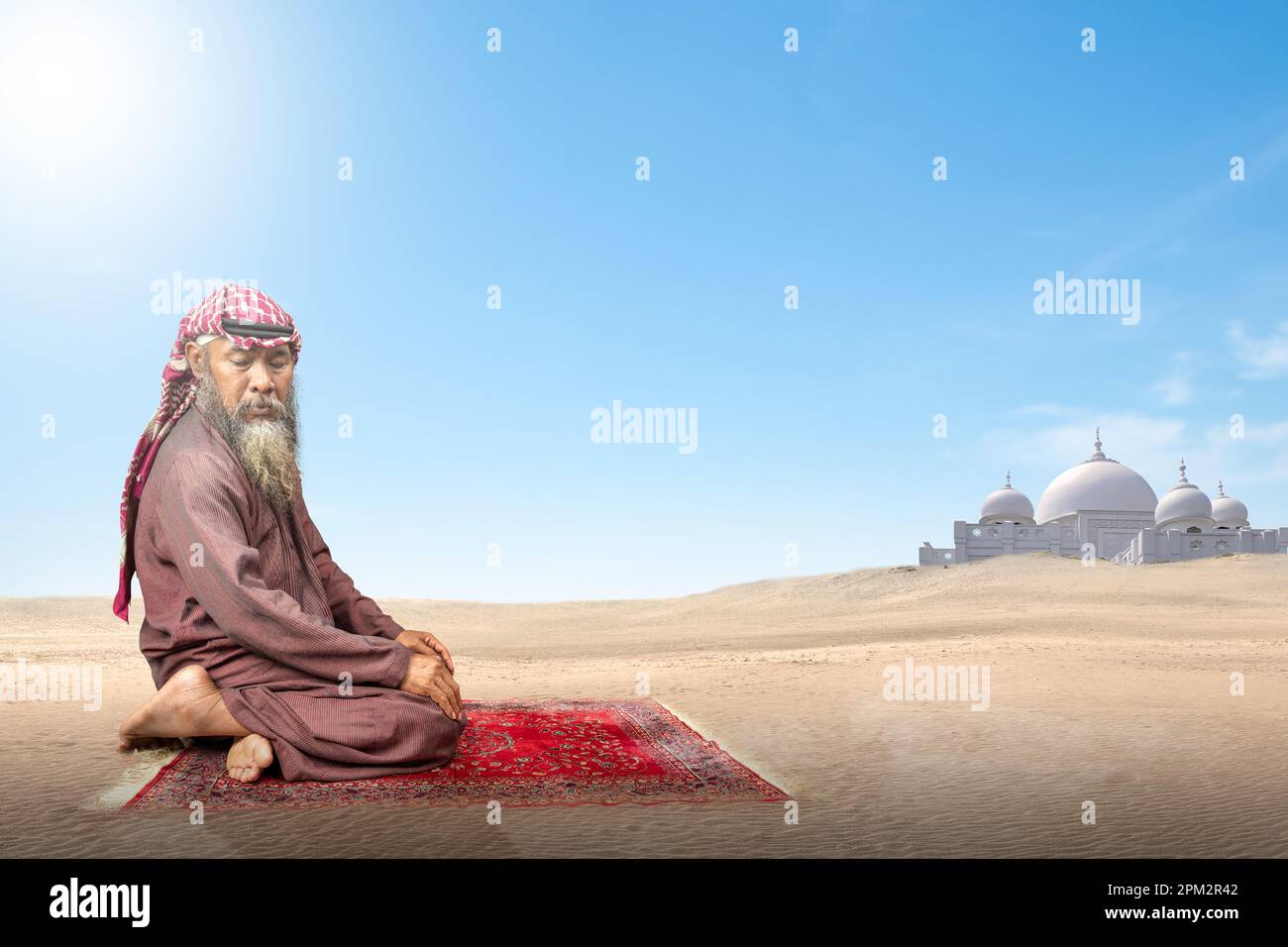 Homme musulman avec une barbe portant du keffiyeh avec agal en position de prière (salat) sur le tapis de prière avec le fond bleu du ciel Banque D'Images