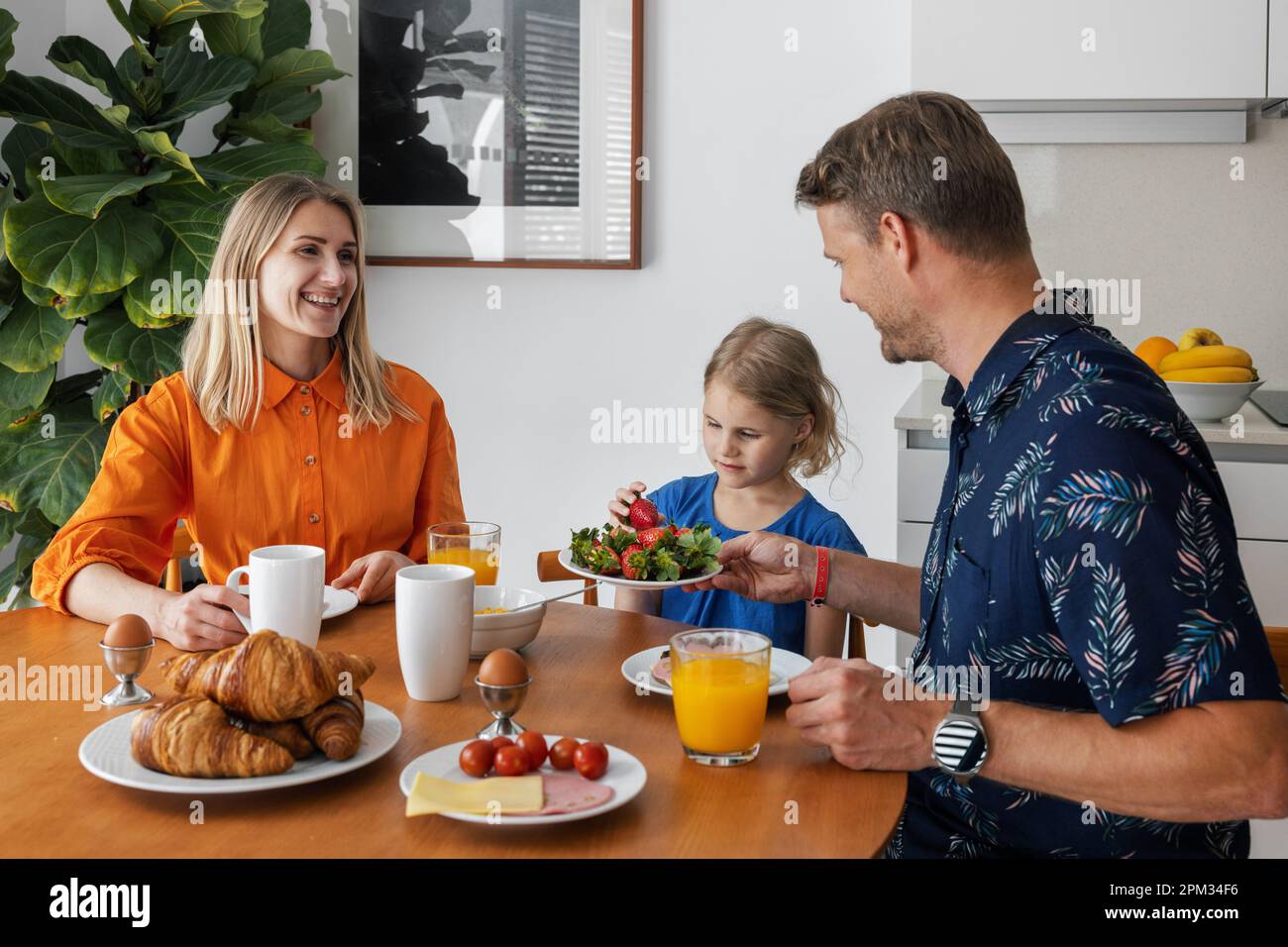 une jeune famille heureuse avec un enfant qui mange un petit déjeuner sain à table dans la cuisine du matin Banque D'Images