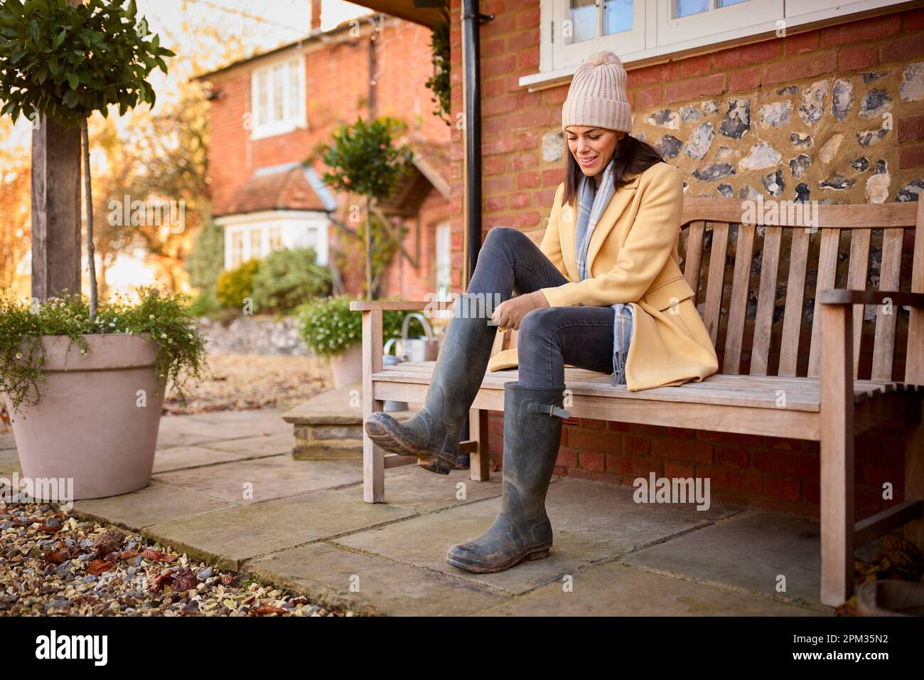 Femme assise sur un banc à l'extérieur de la maison mettant sur des bottes prêtes pour la marche d'automne Banque D'Images