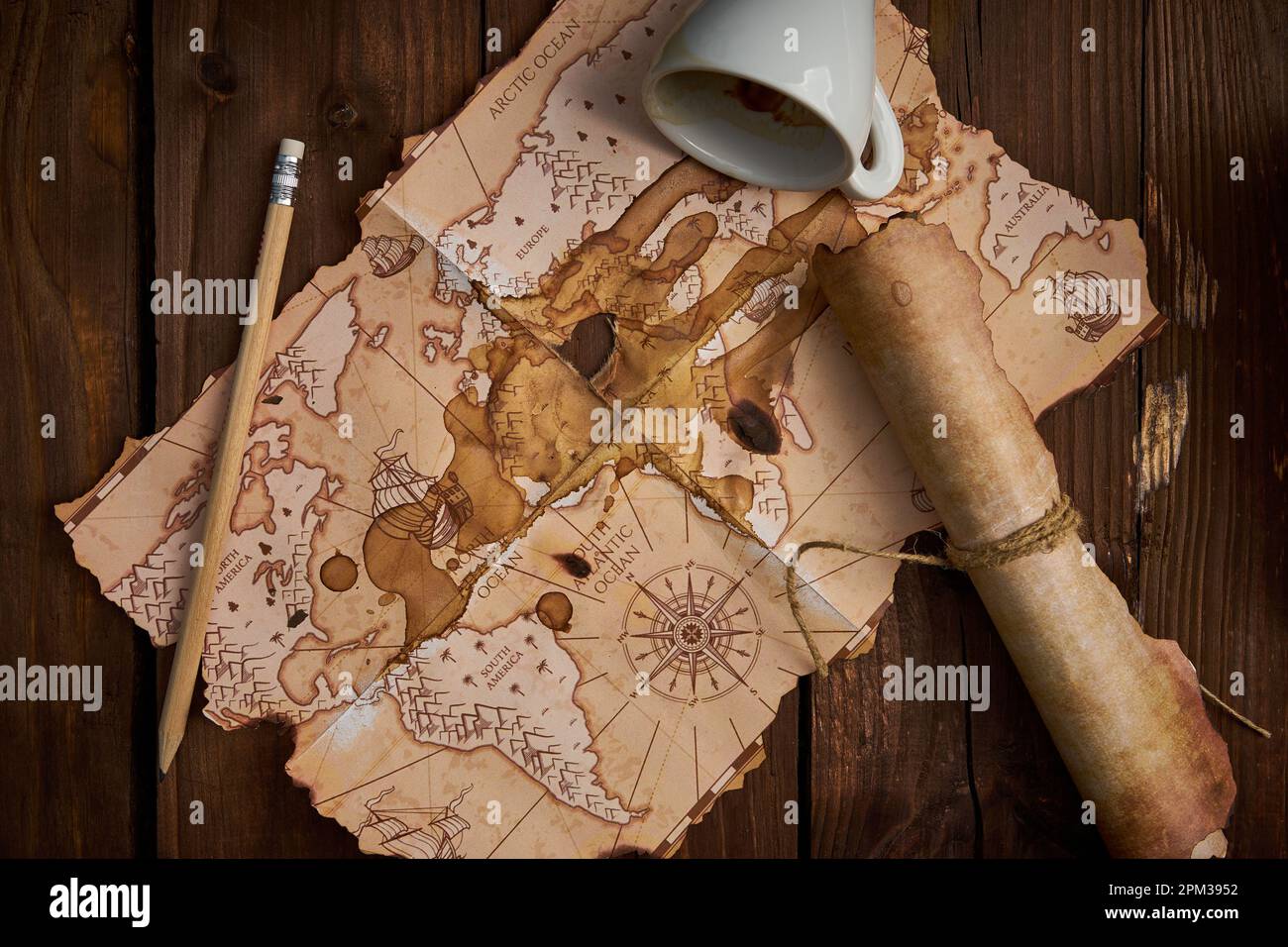 Un vieux parchemin, une vieille carte, un crayon et une tasse de café renversée sur une table en bois. Banque D'Images