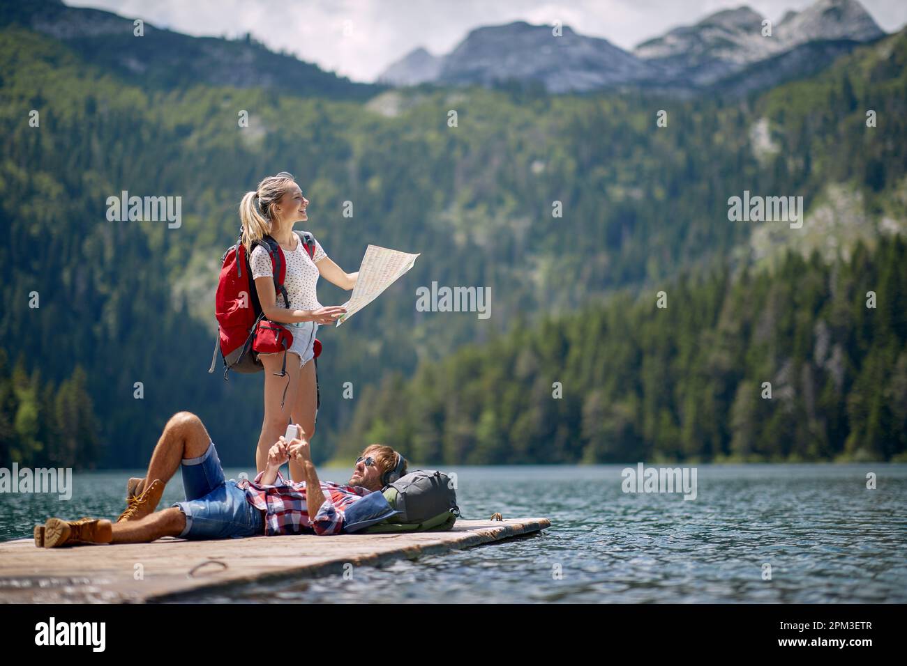 Un jeune couple prend un repos sur le quai au lac lors de la randonnée en montagne par une belle journée. Voyage, nature, randonnée Banque D'Images