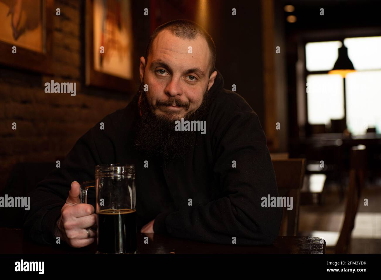 un homme barbu tient un verre de bière tout en étant assis dans un pub. Durée de la bière. Boissons alcoolisées Banque D'Images