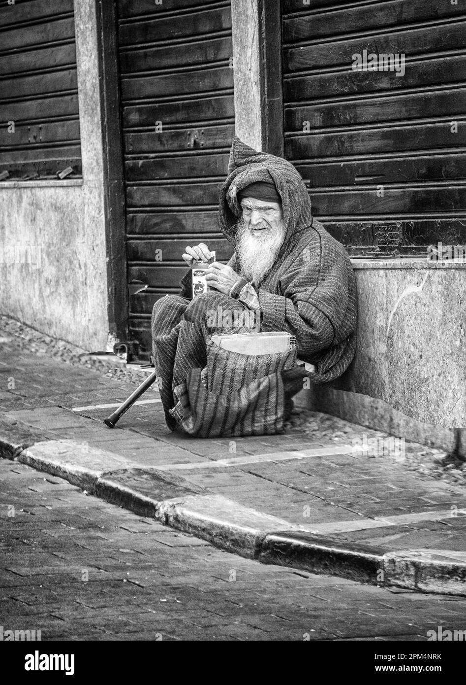 Un homme dans une robe traditionnelle s'accroupille tout en prenant un verre dans une rue de Tanger, au Maroc. Banque D'Images