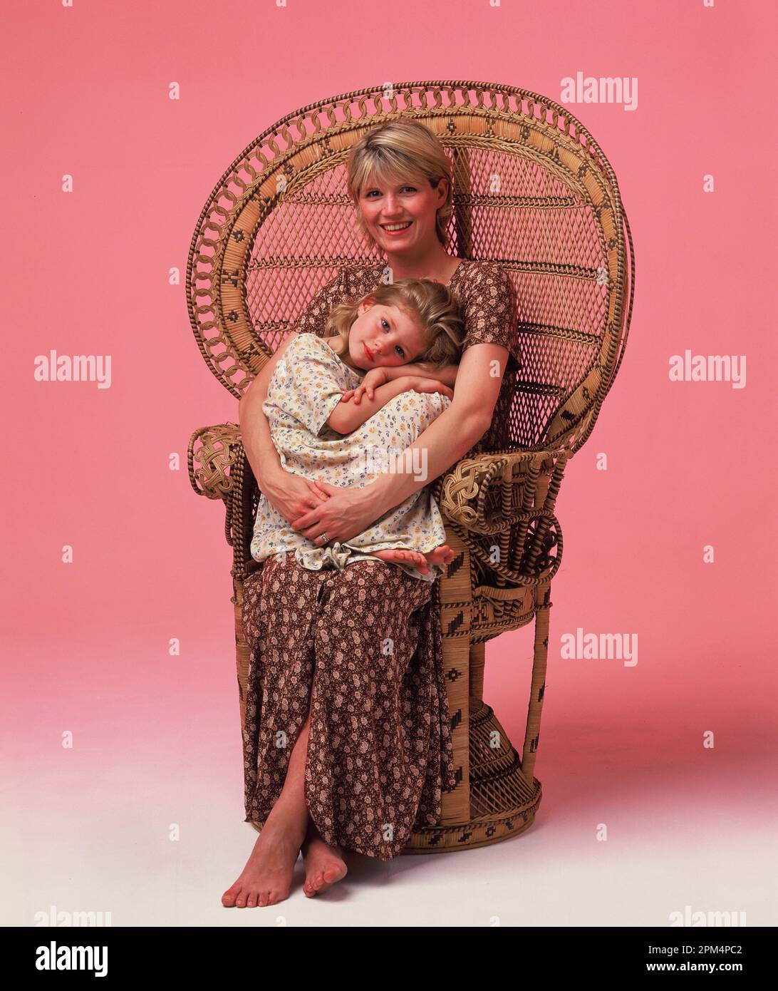 Studio portrait de la jeune mère et de la fille assis dans un fauteuil en rotin. Banque D'Images