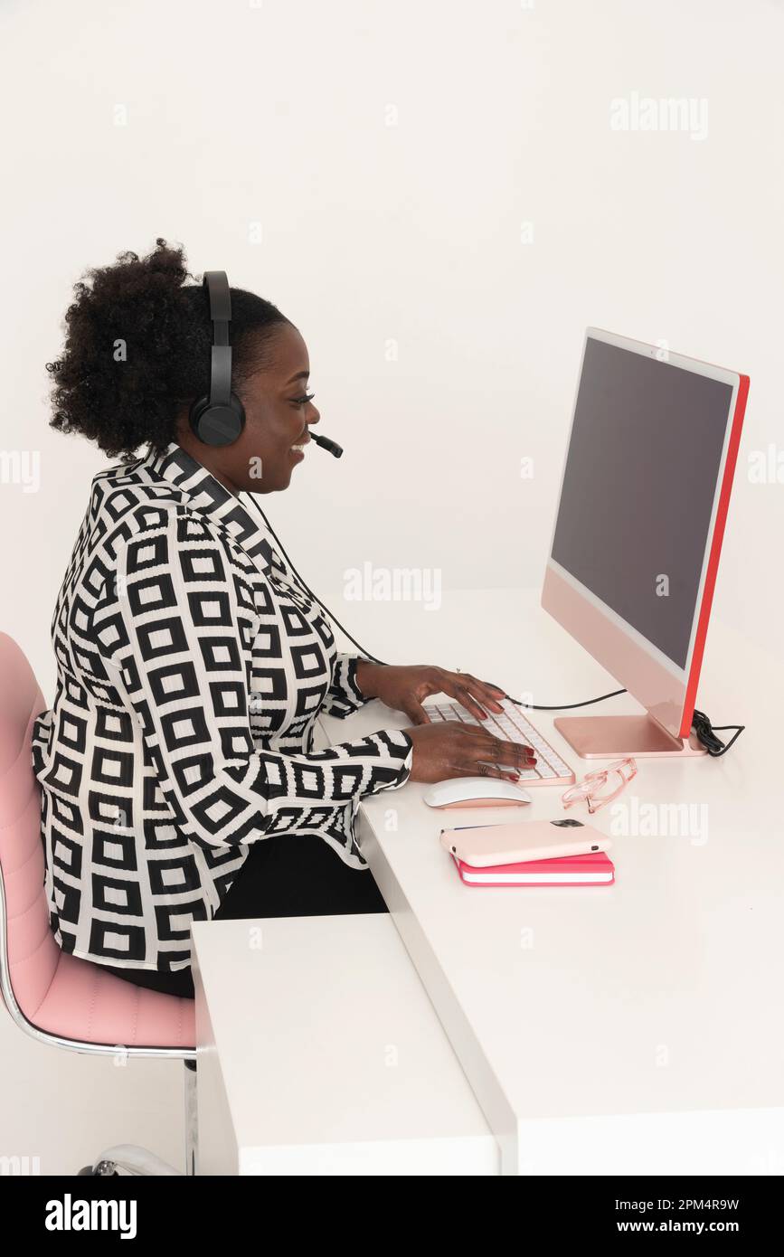 Angleterre, Royaume-Uni. 2023. Femme téléphoniste portant un casque assis à l'ordinateur de bureau avec un grand sourire. Banque D'Images