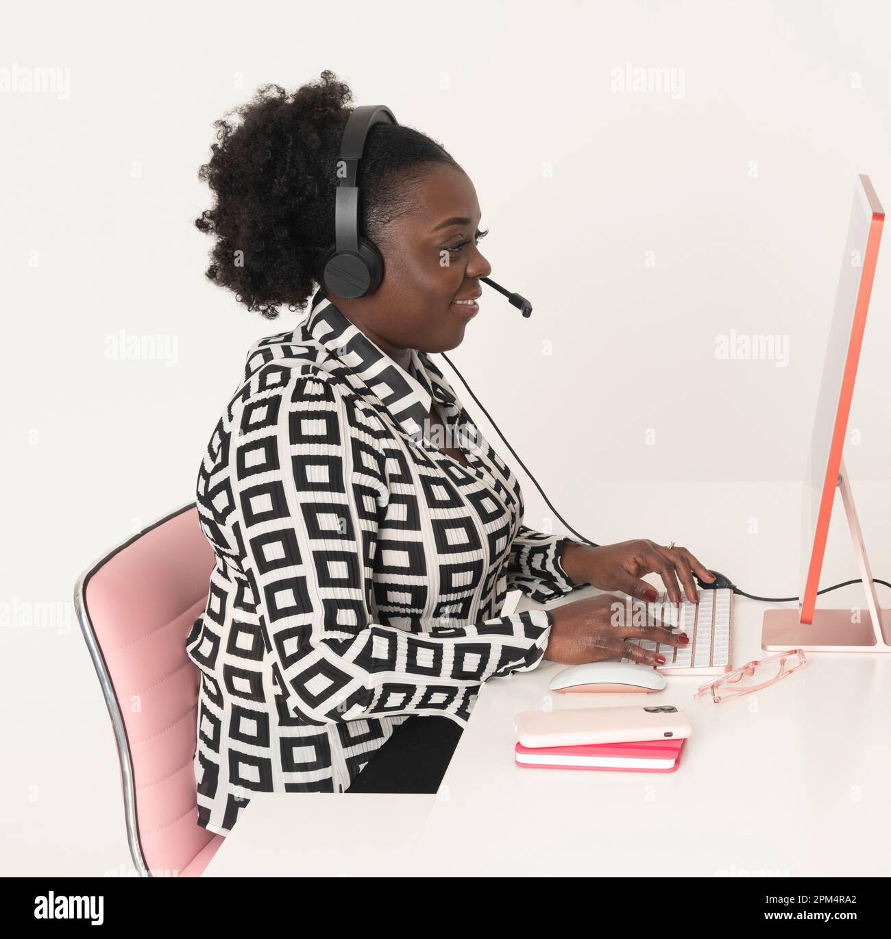 Angleterre, Royaume-Uni. 2023. Femme téléphoniste portant un casque assis à l'ordinateur de bureau avec un grand sourire. Banque D'Images