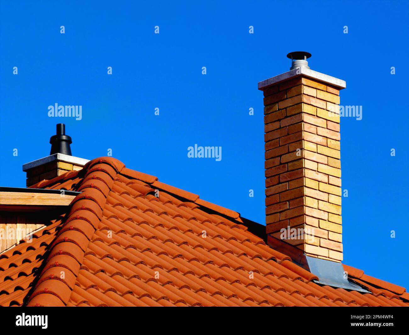 cheminées modernes en briques brunes jaunes avec pierre à chapeau en  céramique blanche, tuiles de toit en argile rouge brun clair et évents en  argile. dormer en bois. ciel bleu clair d'hiver