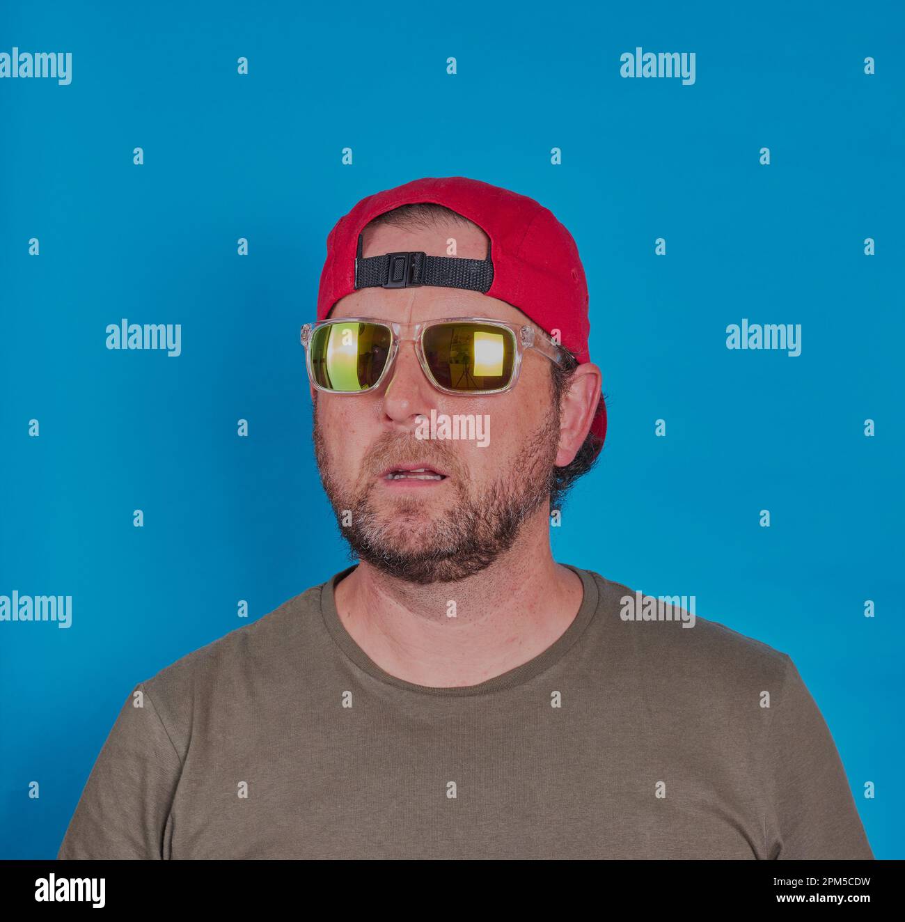 Homme barbu avec lunettes de soleil et casquette sur devant un fond bleu. Autorisation du modèle disponible. Banque D'Images