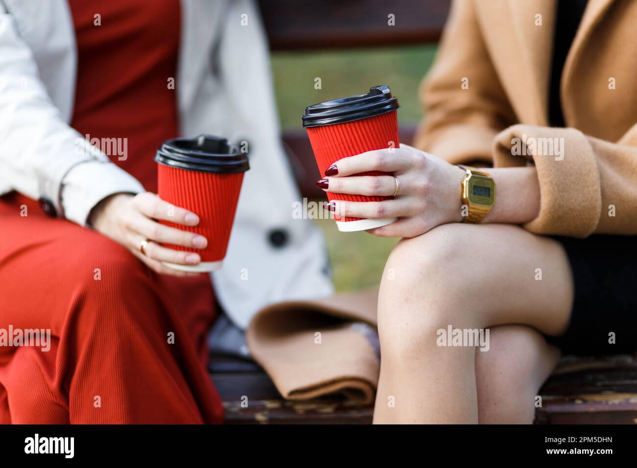 deux femmes tenant des tasses en papier avec des boissons chaudes assis sur un banc Banque D'Images